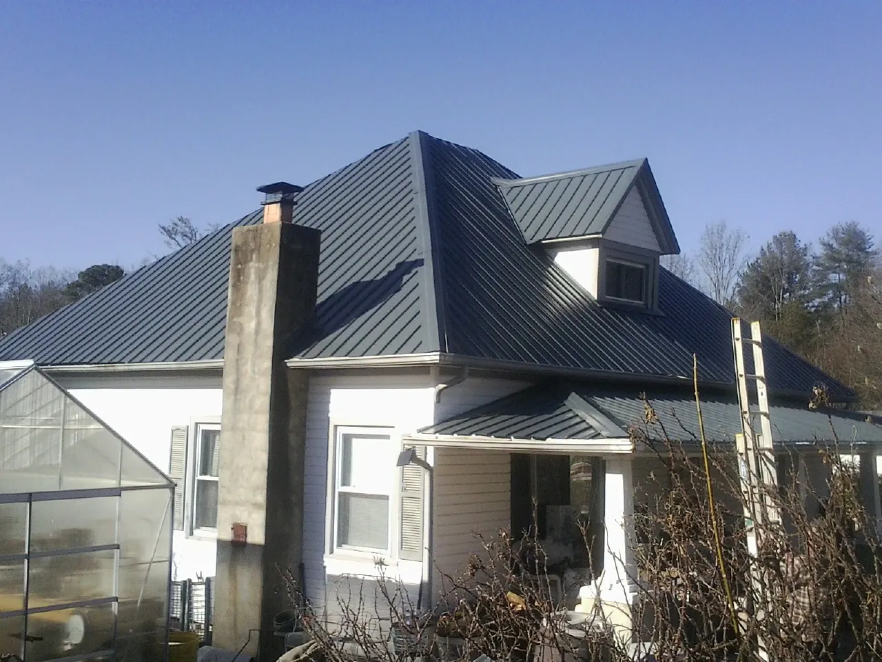 Dark blue standing seam metal roof on a white farmhouse with dormer — Slate & Tile Roof Repair by Roofing Brothers in Franklin Square