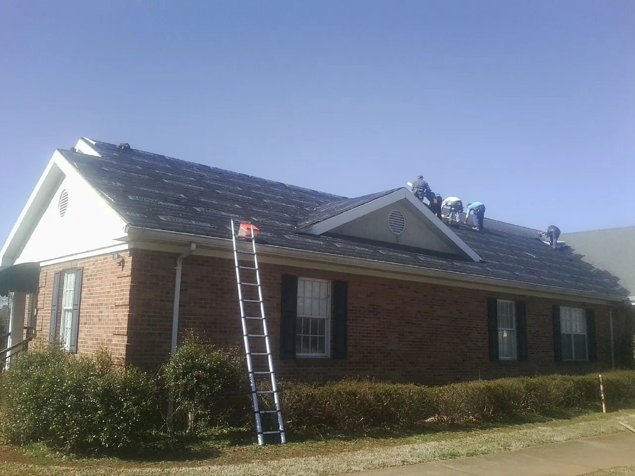 Crew tearing shingles off a brick ranch roof with a ladder set — Emergency Roof Repair work by our crew in Franklin Square