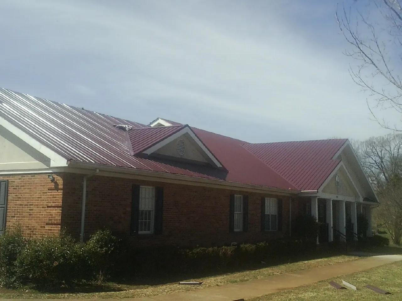 Red metal roof with gabled entries on a long brick building, from a Hail Damage Roof Repair job in Franklin Square
