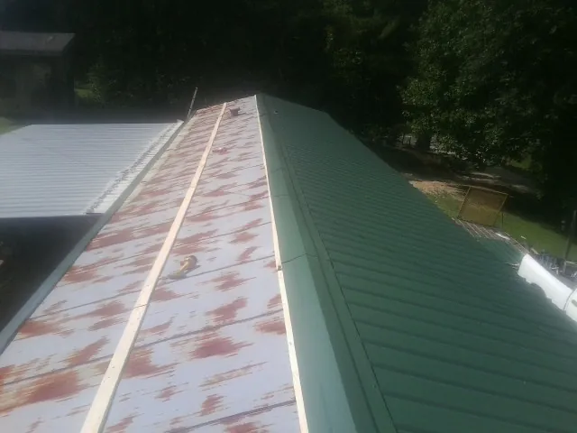 Old rusted panels beside newly installed green metal roofing — Wind Damage Roof Repair by Roofing Brothers in Franklin Square
