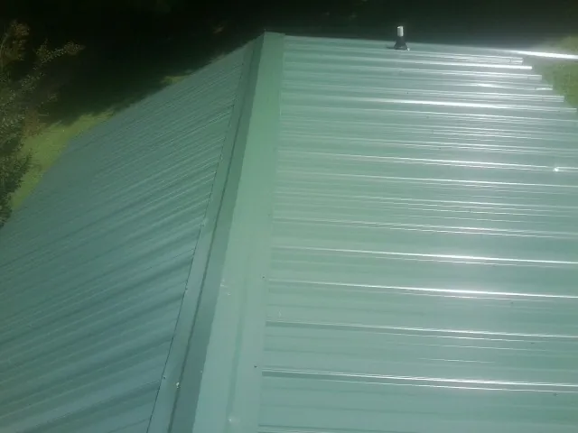 New green metal panels meeting at the ridge of a roof — Flat Roof Repair work by our crew in Franklin Square