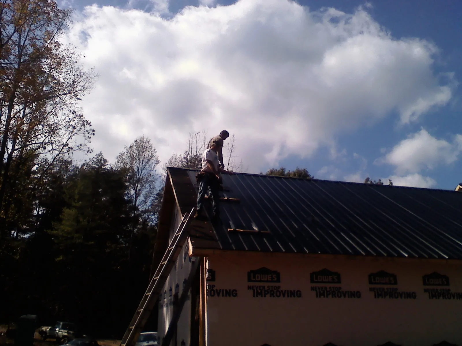 Roofer fastening dark metal panels high against a cloudy sky, from a Roof Inspection job in Franklin Square