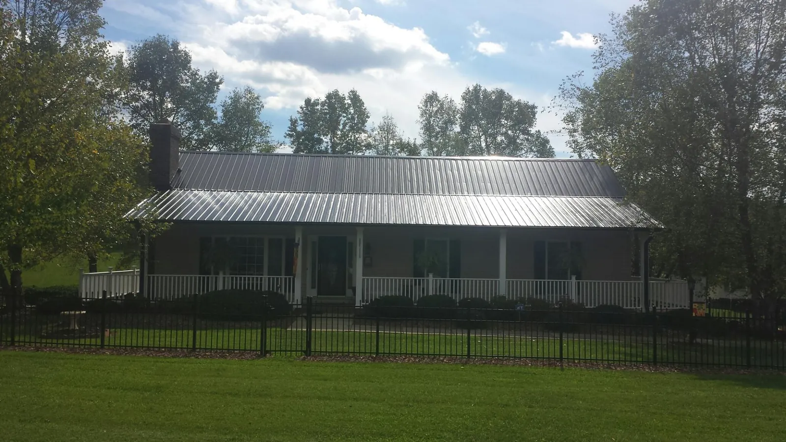 Gray metal roof on a brick ranch with a full width front porch — Gutter Guard Installation work by our crew in Franklin Square